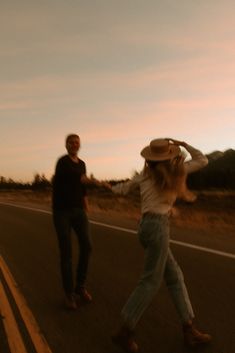 two people are walking down the road with hats on and one person is holding his hat