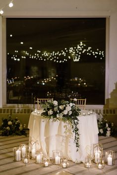 a table with candles and flowers on it in front of a large window at night