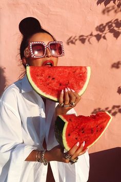 a woman wearing sunglasses and holding two slices of watermelon in front of her face