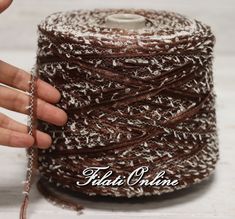 a hand holding a spool of brown and white yarn