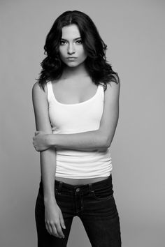 a woman in white shirt and jeans posing with her arms folded over her chest, looking at the camera