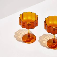 two orange glass candlesticks sitting next to each other on a white table top