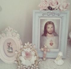 a table topped with pink roses and framed pictures next to a small statue of jesus