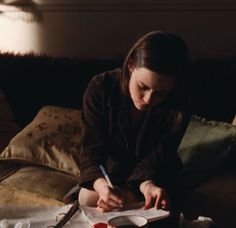 a woman sitting on top of a bed writing in a notebook and holding a pen