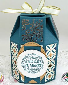 a small blue box with a white ribbon on it and some ornaments around the edges