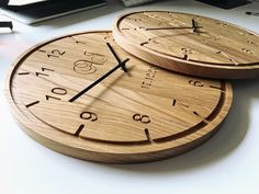 two wooden clocks sitting next to each other on a white table with computer equipment in the background