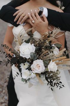 a bride and groom hugging each other with their wedding rings in their hands, while the bouquet is surrounded by greenery