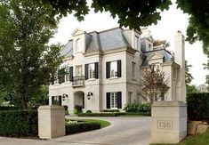 a large white house with lots of windows and bushes in front of the entrance to it