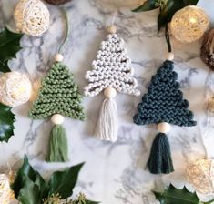 crochet christmas tree ornaments are displayed on a marble surface with greenery and lights