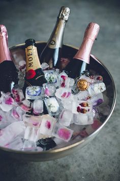 three bottles of champagne and ice cubes in a metal bowl on the floor next to each other