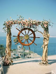 a wooden steering wheel decorated with flowers and greenery for an outdoor wedding ceremony by the ocean