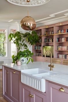 a kitchen with pink cabinets and white counter tops, gold faucet lights above the sink