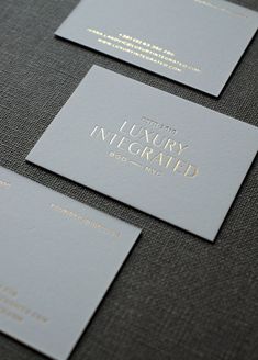 three silver business cards with gold foil on the front and back, sitting on a gray surface