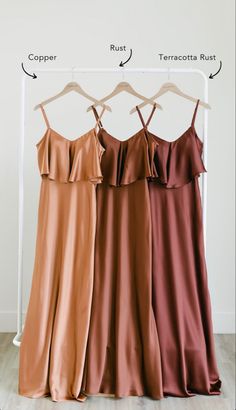 three dresses hanging on a rack in front of a white wall and wood flooring