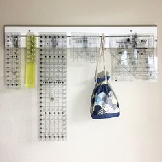 two bags hanging from hooks on a wall next to a ruler and measuring tape holder