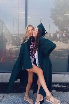 two young women in graduation gowns posing for a photo outside the glass building with their arms around each other