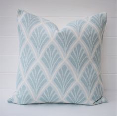 a light blue and white pillow on a white brick wall with an intricate design in the middle