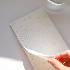 a person holding a piece of paper on top of a white table next to a cup