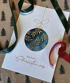 a christmas ornament hanging from a ribbon on top of a card with the words merry christmas