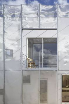 a white building with glass walls and a wooden chair on the balconi balcony