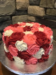 a cake decorated with red and white flowers on top of a silver platter next to a stone wall