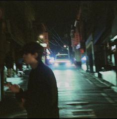 a man standing on the side of a street at night with a cell phone in his hand