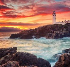 a lighthouse on top of a rocky shore with waves crashing in front of it at sunset