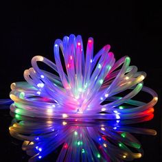 a colorful light up flower on a black surface with reflections in the water and dark background