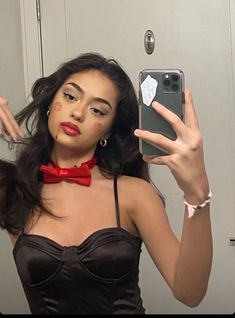 a woman wearing a red bow tie taking a selfie in the mirror with her cell phone