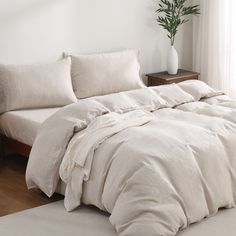 an unmade bed with white linens in a room next to a wooden table