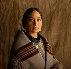 a native american woman wearing a shawl and looking off to the side in front of a brown background