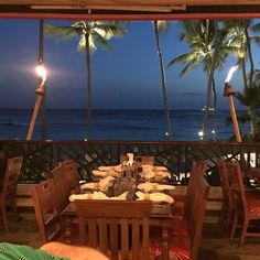 an outdoor dining area with tables and chairs overlooking the ocean at night, lit by lamps