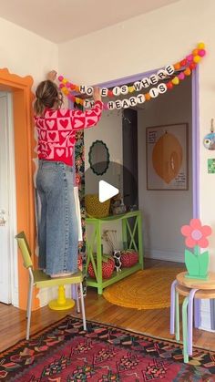 a woman standing on top of a chair in front of a colorful wall hanging from the ceiling