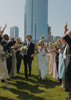 a bride and groom walk through the grass with their wedding party in front of them