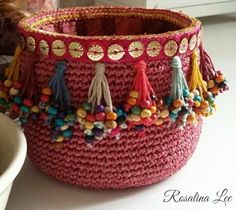 a pink crocheted basket with tassels and beads on the inside is sitting next to a white bowl