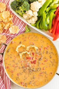 a bowl of soup next to some vegetables and chips