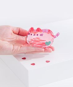 a hand holding a pink cat shaped object on top of a white box with polka dots