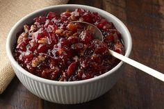 a white bowl filled with cranberry sauce on top of a wooden table next to a spoon