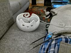 a dog laying on the floor next to a bowl with yarn in it and needles