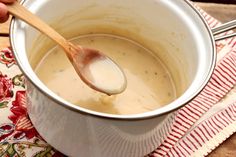 a wooden spoon in a white pot filled with soup on a red and white napkin