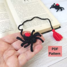 a hand holding a small black spider on top of a book with red tassels