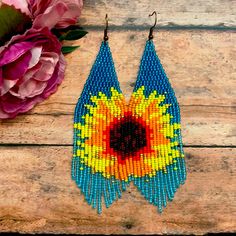 a pair of beaded earrings sitting on top of a wooden table next to flowers