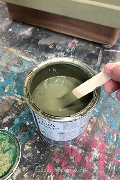 a person holding a paintbrush over a can of green paint