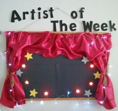 a sign that says artist of the week hanging from a wall with lights on it