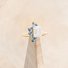 a ring with an emerald and blue topazte surrounded by small diamonds on a wooden stand