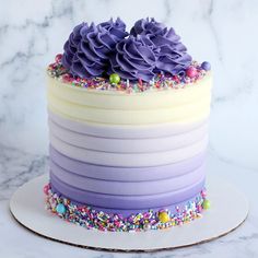 a multi layer cake with purple frosting and sprinkles on the top