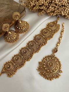 two pieces of gold jewelry on a white cloth with beads and flowers in the background