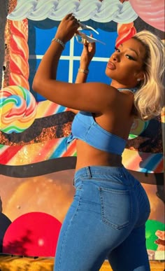 a woman in tight jeans and crop tops is holding scissors to her hair while standing next to a colorful backdrop