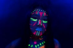 a woman with neon paint on her face and body is shown in the dark blue light