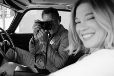 a man and woman sitting in a car taking pictures